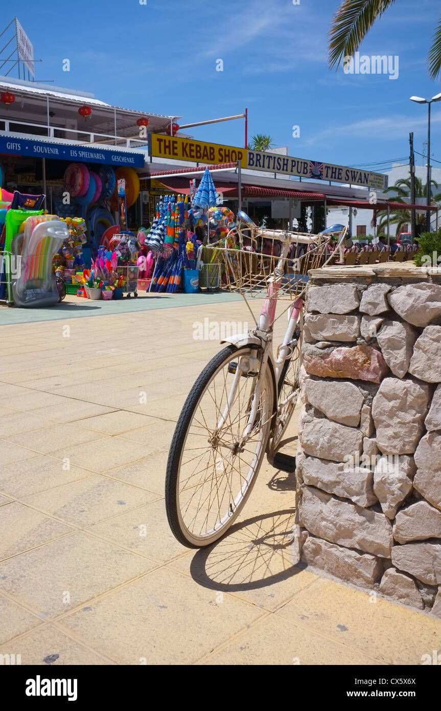 ein altes Fahrrad links am Strand vor Geschäften und Bars auf Mallorca Stockfoto