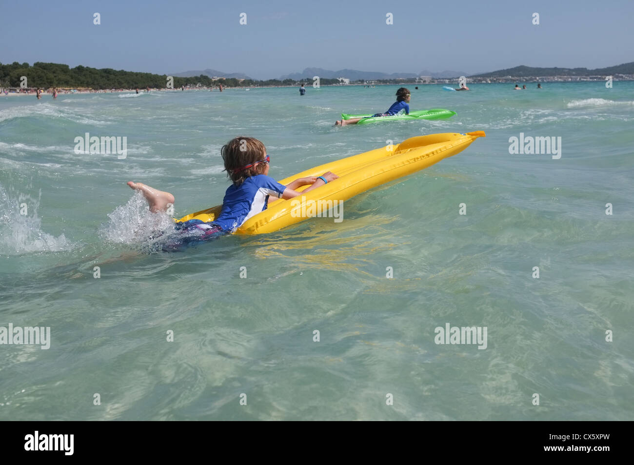 Jungen spielen am Strand in den Wellen auf aufblasbaren Luftmatratzen Stockfoto