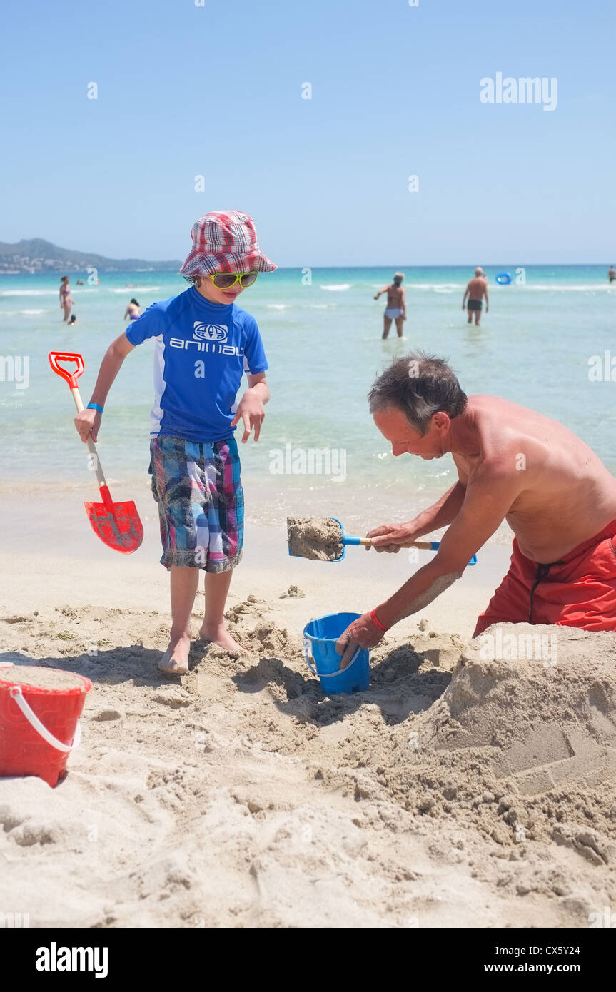 ein kleiner Junge und sein Großvater spielt am Strand Sandburgen zu graben Stockfoto