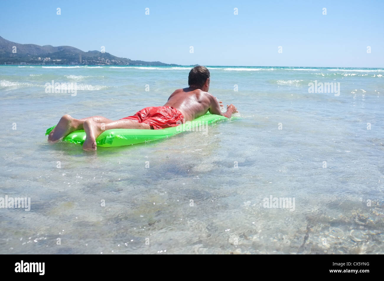 ein Mann entspannt sich in den Wellen auf der Insel Mallorca auf einem Lilo an einem Sandstrand in der warmen Sonne Stockfoto