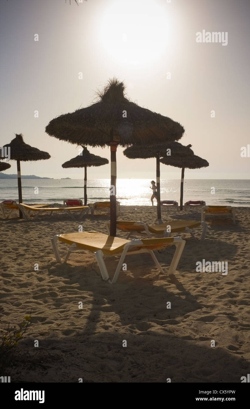 ein einsamer Läufer an einem leeren Strand wie die Sonne aufgeht läuft vorbei an Sonnenliegen und Stühle Stockfoto