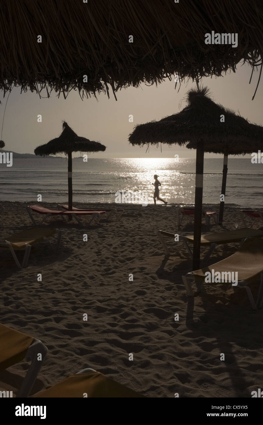 ein einsamer Läufer läuft am Strand von Alcudia Mallorca, als die Sonne am Morgen aufgeht Stockfoto