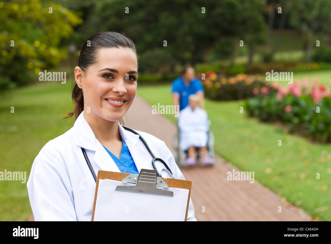 freundliche Ärztin Portrait im Freien ist Hintergrund ihrer Kollegin Patienten im Rollstuhl schieben Stockfoto