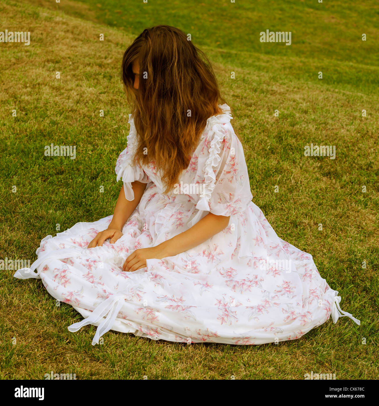 eine Frau in einem geblümten Kleid sitzt auf einer Wiese Stockfoto