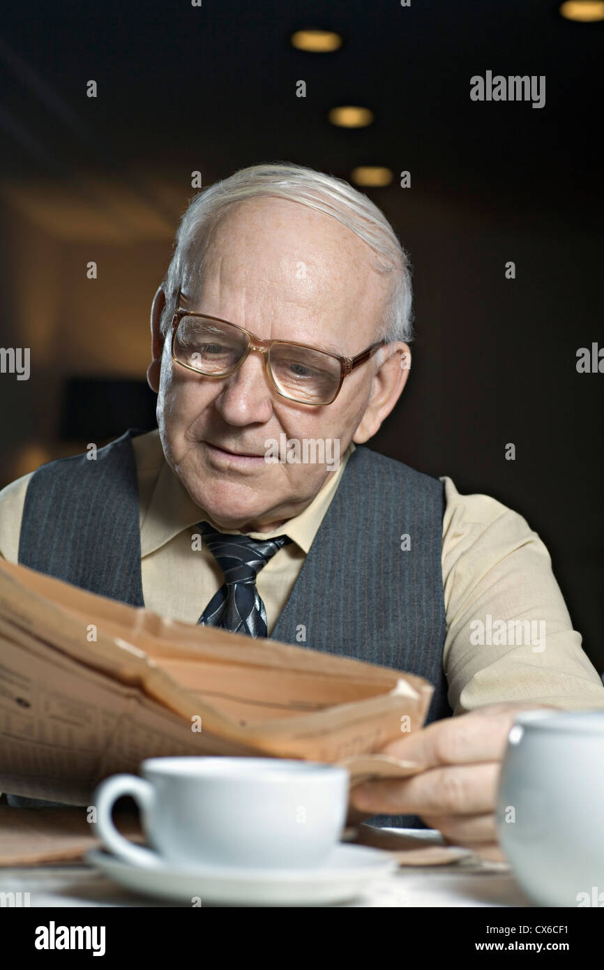 Ein senior Mann liest eine Zeitung in einem café Stockfoto