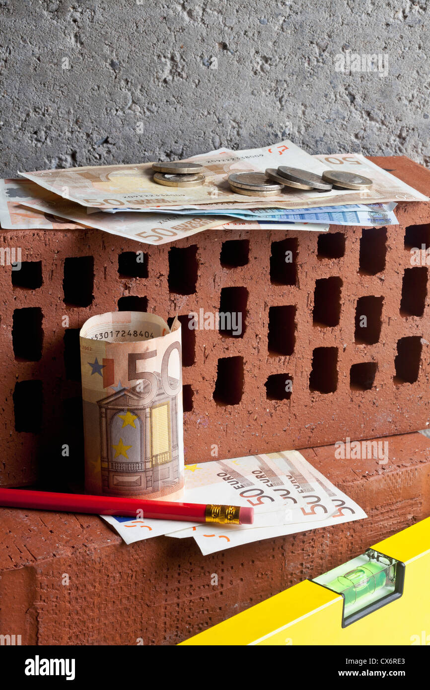 Einen Haufen Geld auf gestapelten Ziegelsteinen mit einem Bleistift und Ebene Stockfoto