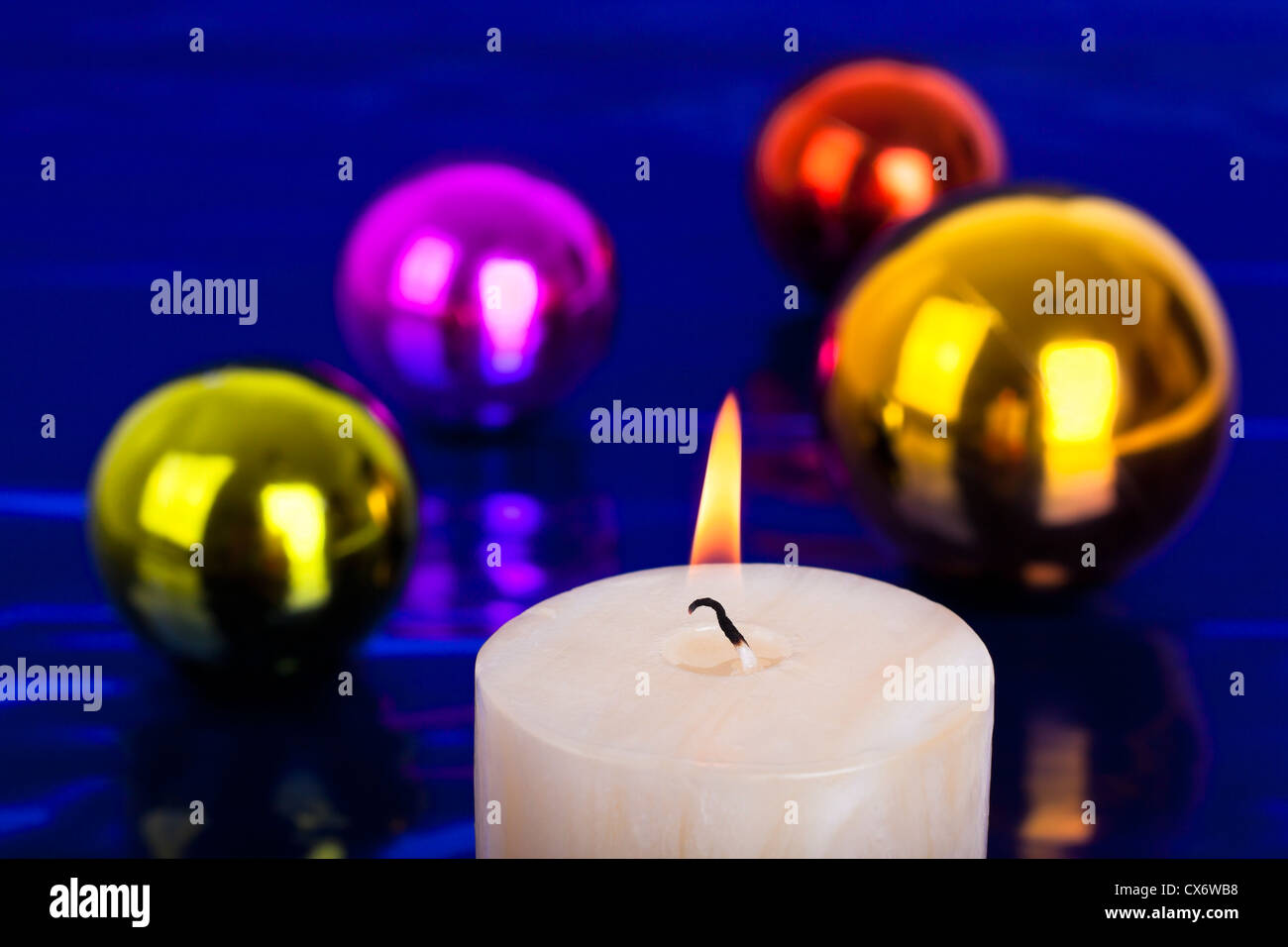 Nahaufnahme von Weihnachtskerze und bunten Kugeln über glänzenden blauen Hintergrund. Stockfoto