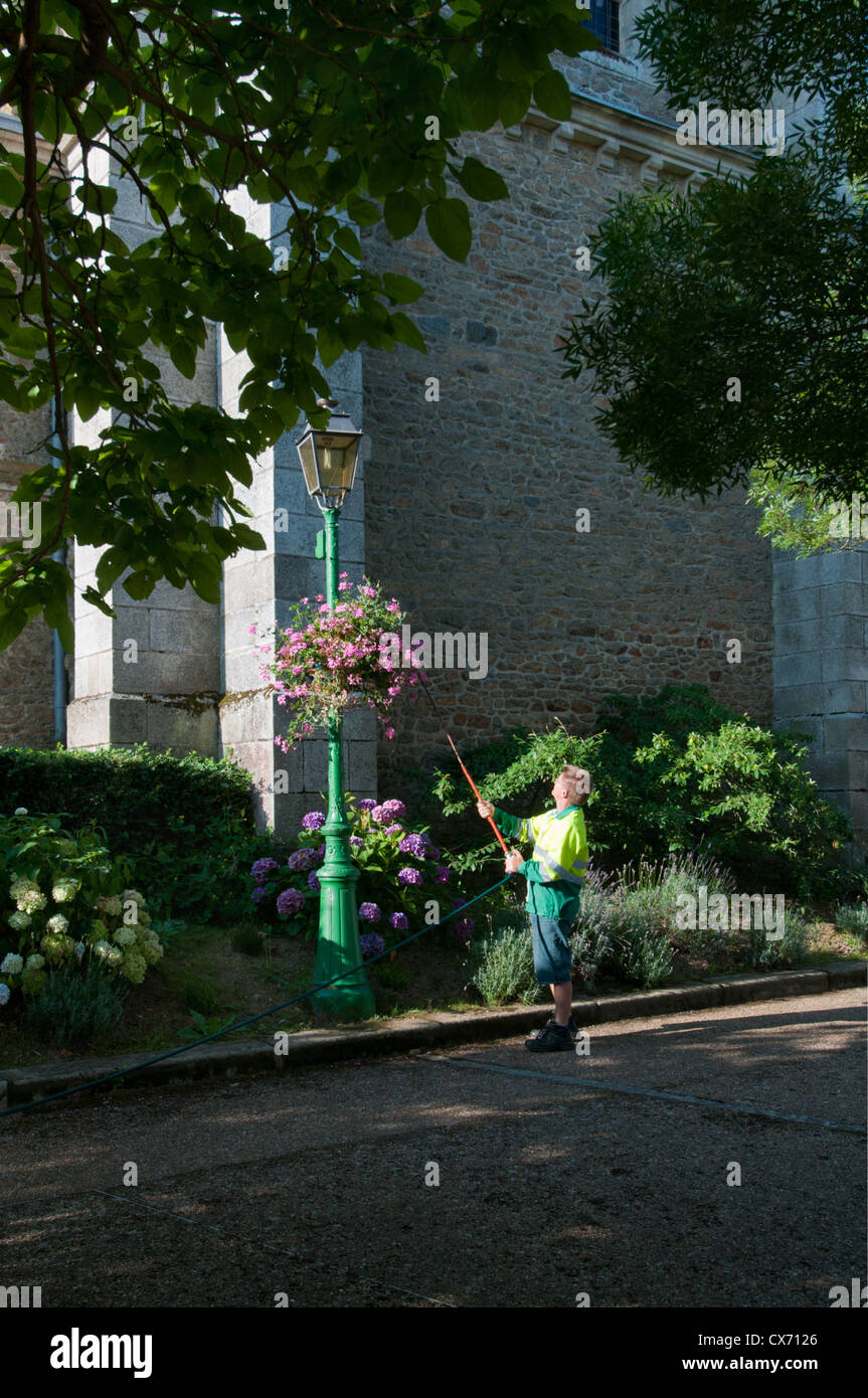 Mann Bewässerung Blumenampel in Saint-Pierre-des-Nids Village, Mayenne, Pays De La Loire, Frankreich. Europa. Stockfoto