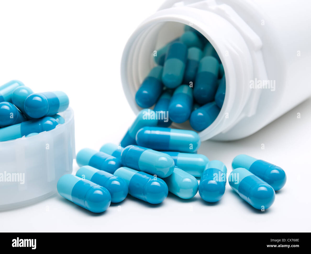 Viele blaue Pillen und Kunststoffbehälter auf weißem Hintergrund. Stockfoto