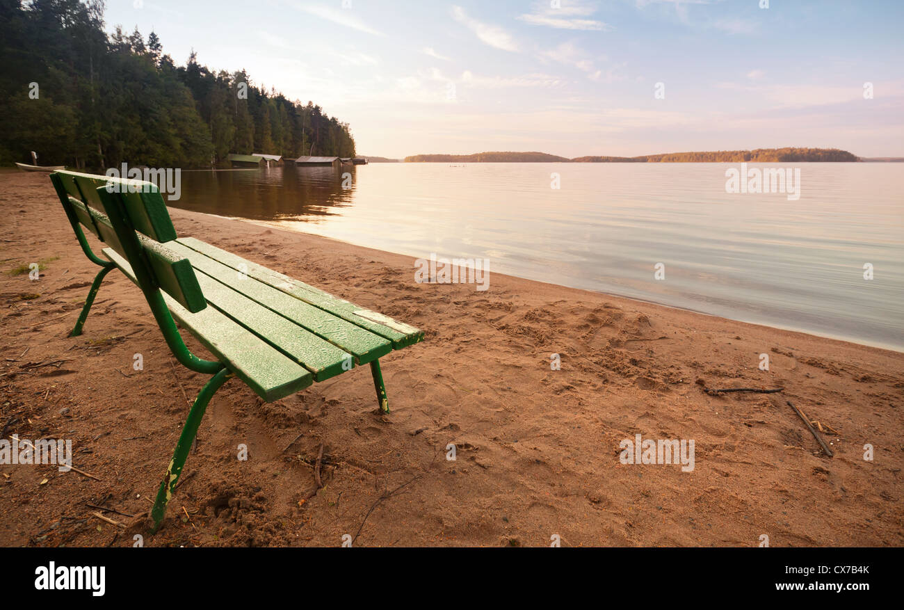 Grüne Holzbank an der Küste des Sees im Morgenlicht Stockfoto