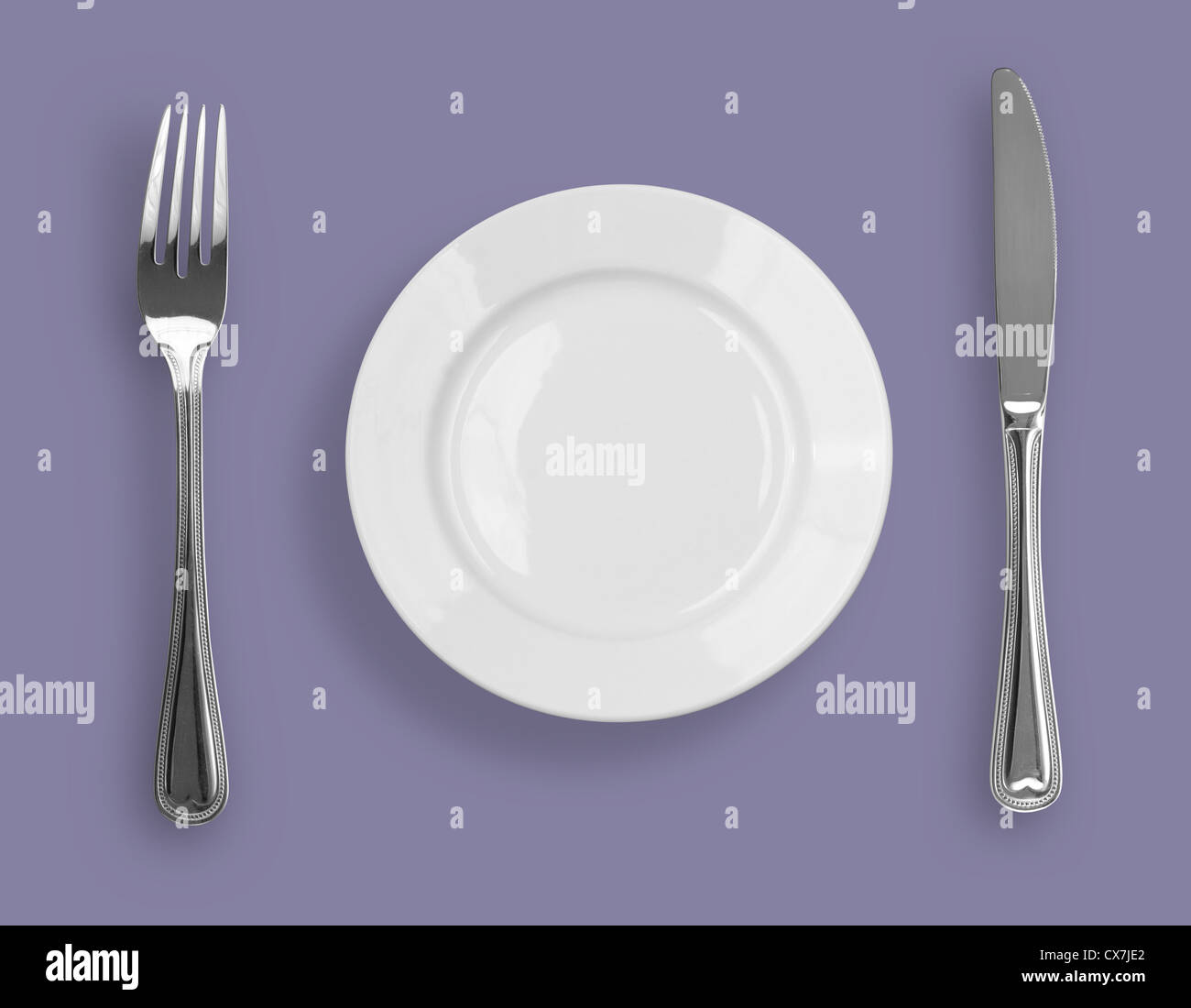 Teller, Messer und Gabel auf violettem Hintergrund Stockfoto