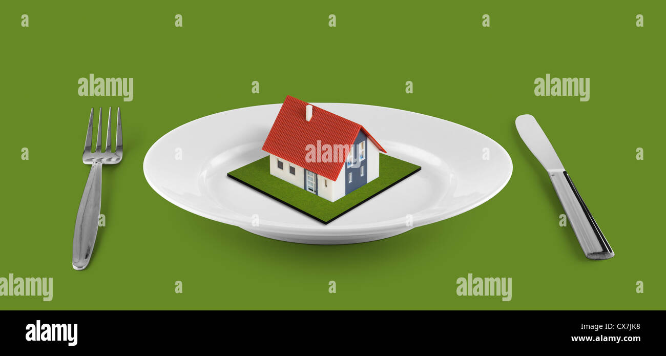 kleines Haus-Konzept auf weißen Teller befindet sich am grünen Tisch Stockfoto
