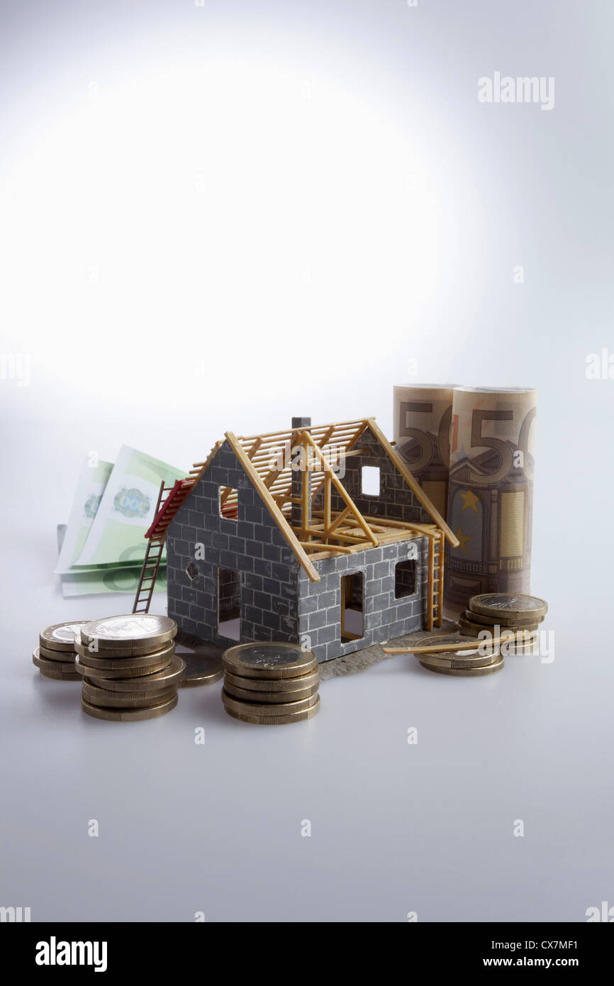 Ein teilweise gebauten Haus mit EU-Währung und Münzen um ihn herum Stockfoto