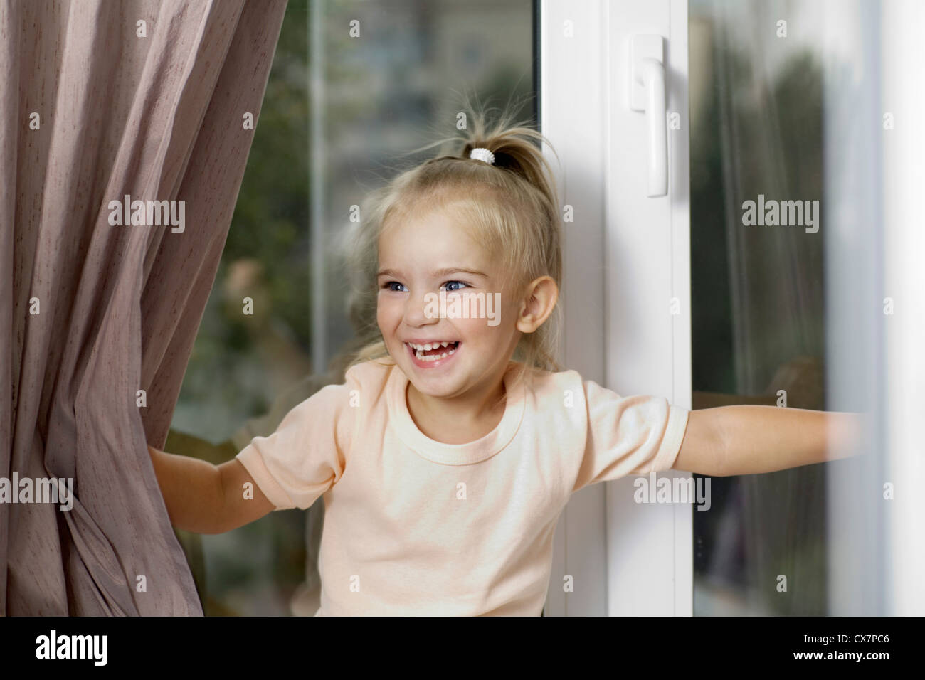 Ein lachendes Mädchen auseinanderdrücken Fenstervorhänge Stockfoto