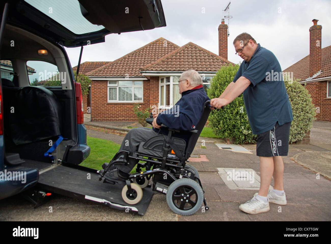 Männliche Pflegekraft Sohn schob einen behinderten älteren Mann im Rollstuhl auf eine eingebaute Rampe in ein speziell angepasstes Auto für immer über Stockfoto