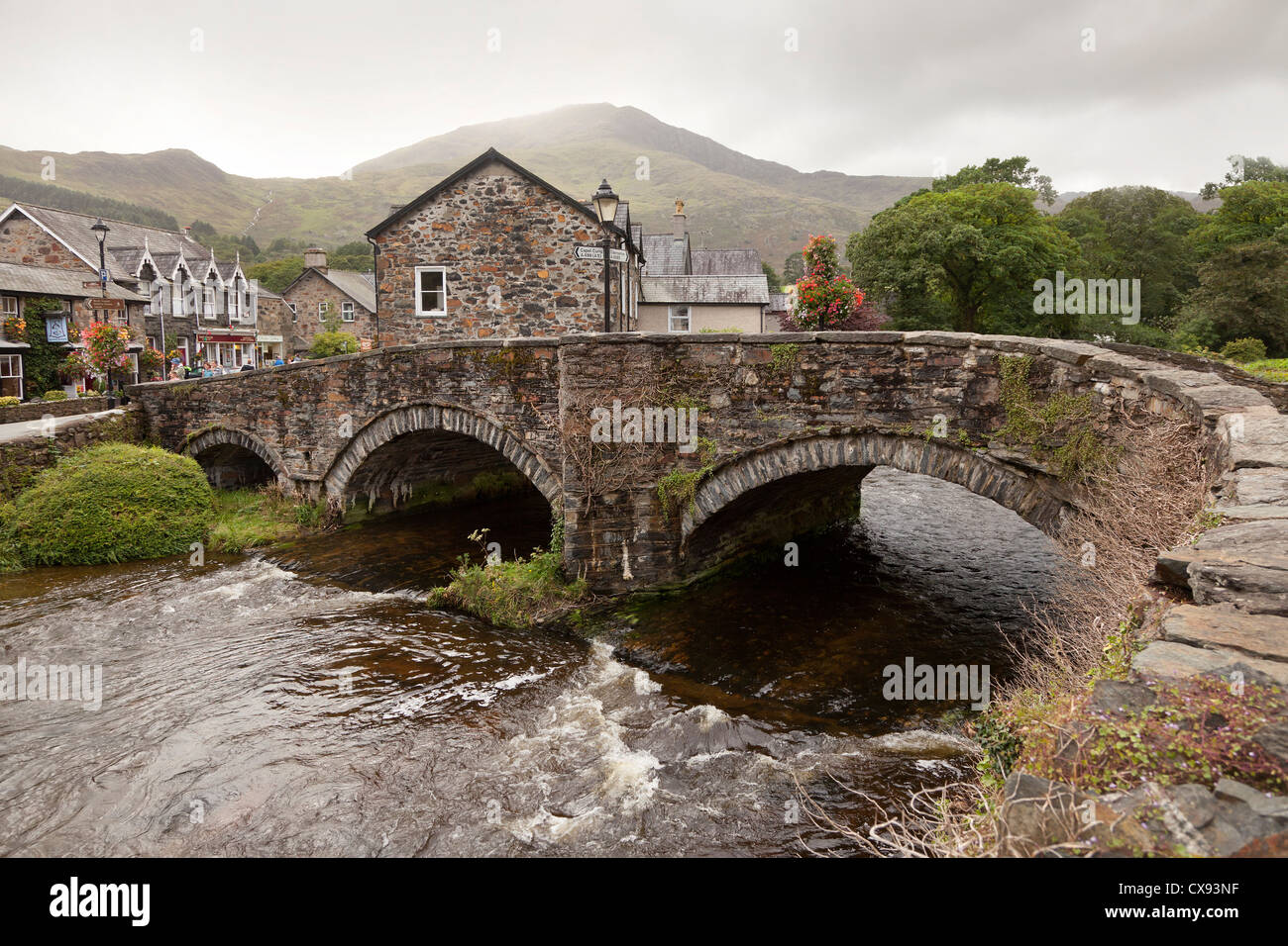Eine alte Steinbrücke mit zwei Bögen in Beddgelert Dorfzentrum, Wales. Stockfoto