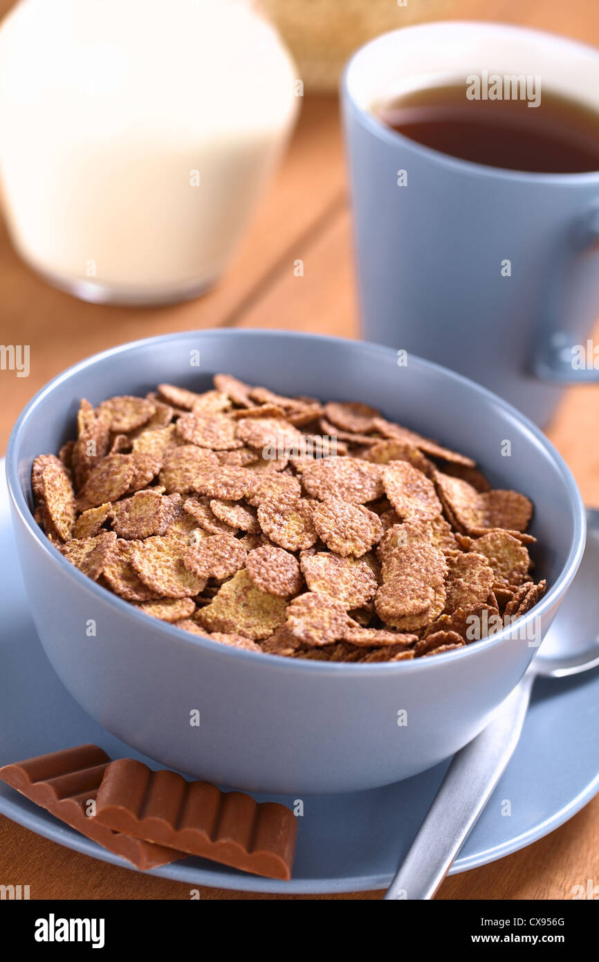 Schüssel Müsli Schoko Cornflakes mit Löffel und Schokolade Bars, eine Tasse Tee und einen Krug Milch in den Rücken Stockfoto