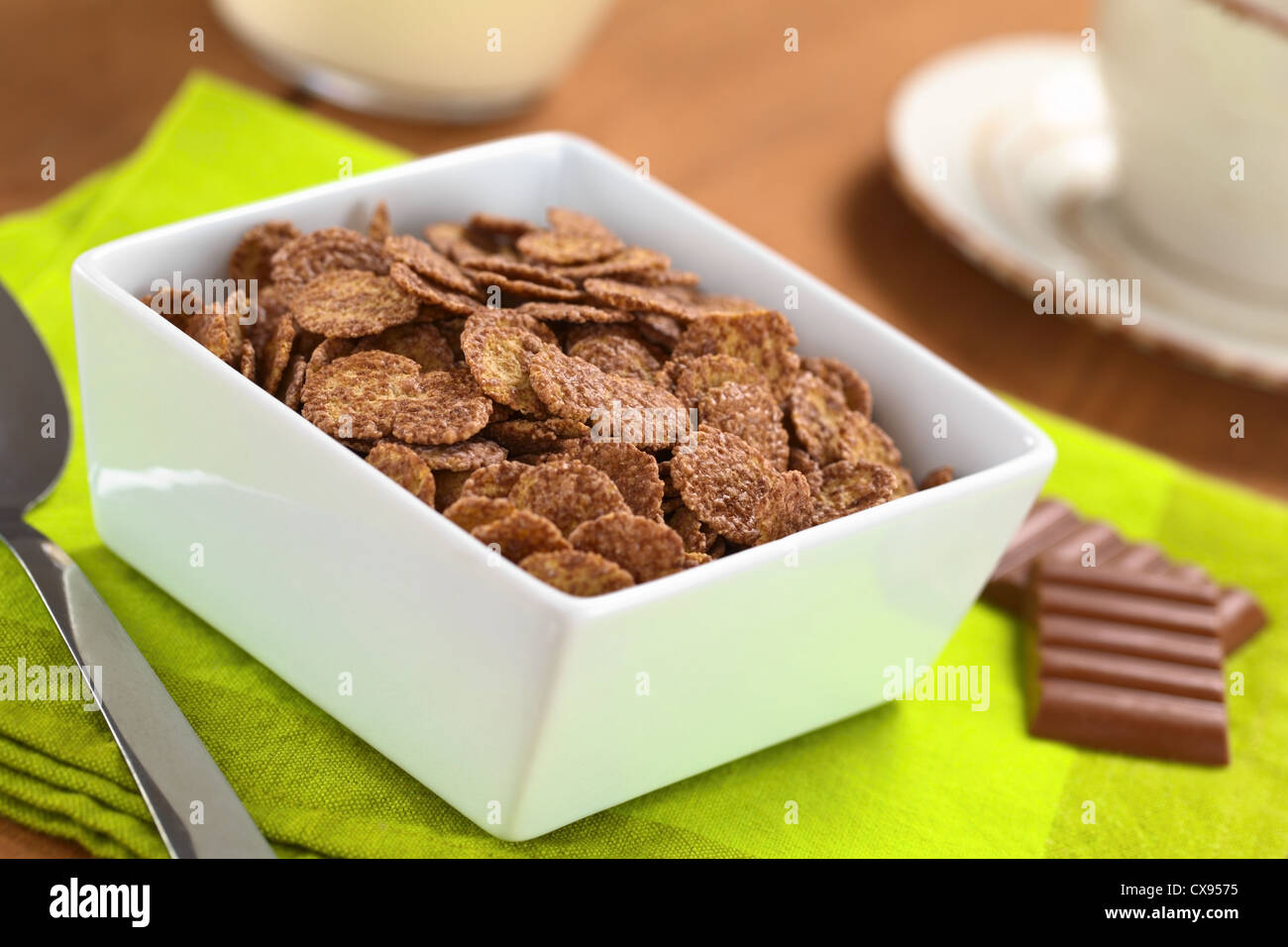 Schüssel Müsli Schoko Cornflakes mit Milch in den Rücken, die Löffel und Schokolade Bars und eine Tasse Stockfoto