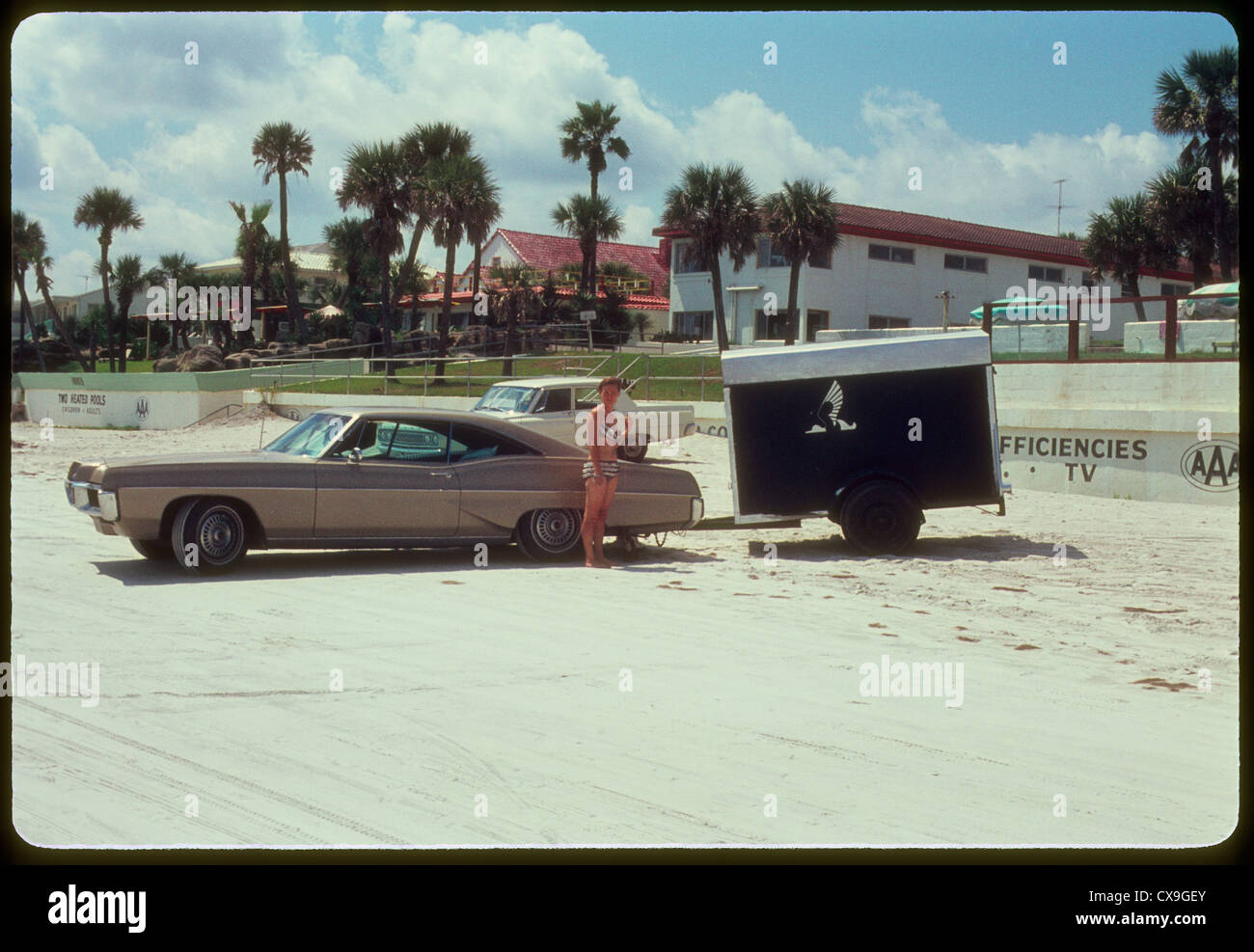 Frau stehend auf Daytona Beach neben Auto 1968 1960s Bikini Sommer Urlaub Florida Tourist Tourismus Stockfoto