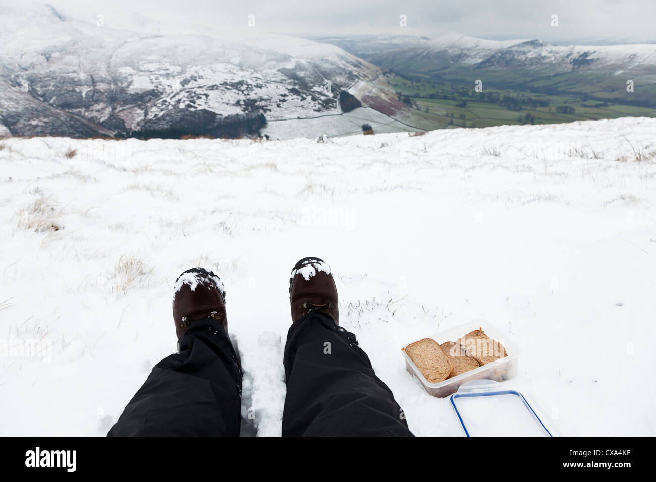 Walker essen ein Lunchpaket mit Sandwiches und saß in der Landschaft Schnee im Winter, Derbyshire, Peak District, England, Großbritannien Stockfoto