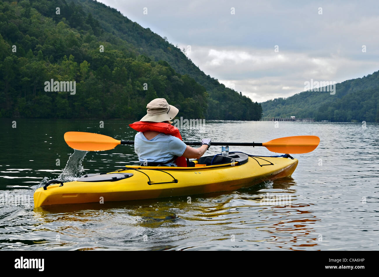 Eine Frau mit Hut, mit dem Kajak auf einem ruhigen See und Schwimmweste. Stockfoto