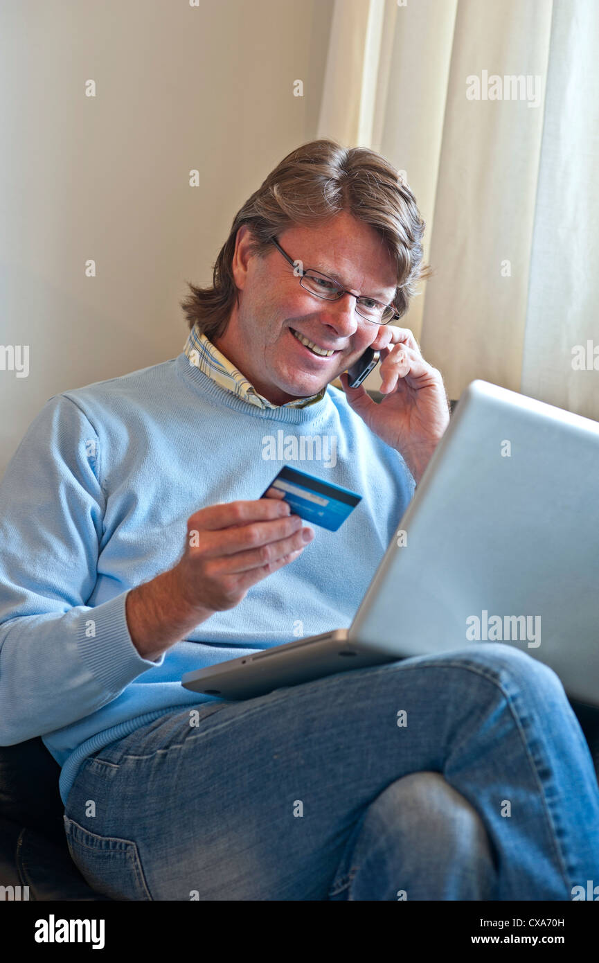 Reifer Mann zu Hause, eine finanzielle Transaktion zu verdienen online mit seinem Laptop und ein iPhone 4 s-smartphone Stockfoto