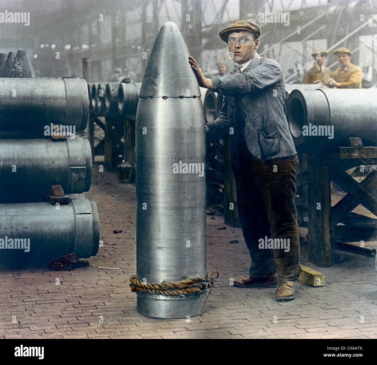 Koloriertes Foto eines männlichen Arbeiters, der neben einer großen Muschel in einer Munitionsfabrik, England, 1918, steht. (Foto von Burton Holmes) Stockfoto