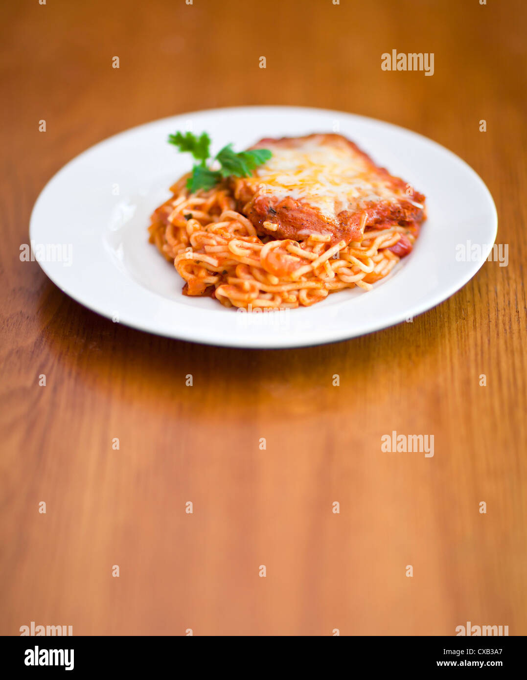Chicken parmigiana auf einem weißen Teller und Tisch aus Holz Stockfoto