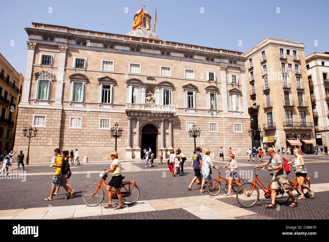 Eine Gruppe von Touristen mit leuchtend orangefarbenen Fahrräder Traverse über La Place Sant Jaume, einem historischen Plaza der Gebäude des Bundes Stockfoto