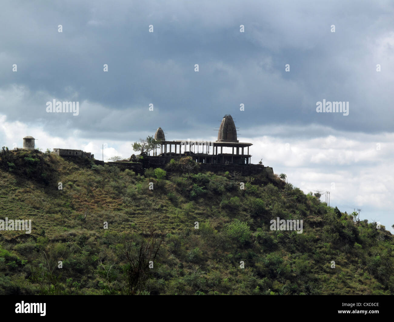 Die Struktur eines verlassenen Tempels auf einem grünen Hügel mit dicken Wolken am Himmel auf dem Weg zum Vaishno Devi in Indien Stockfoto