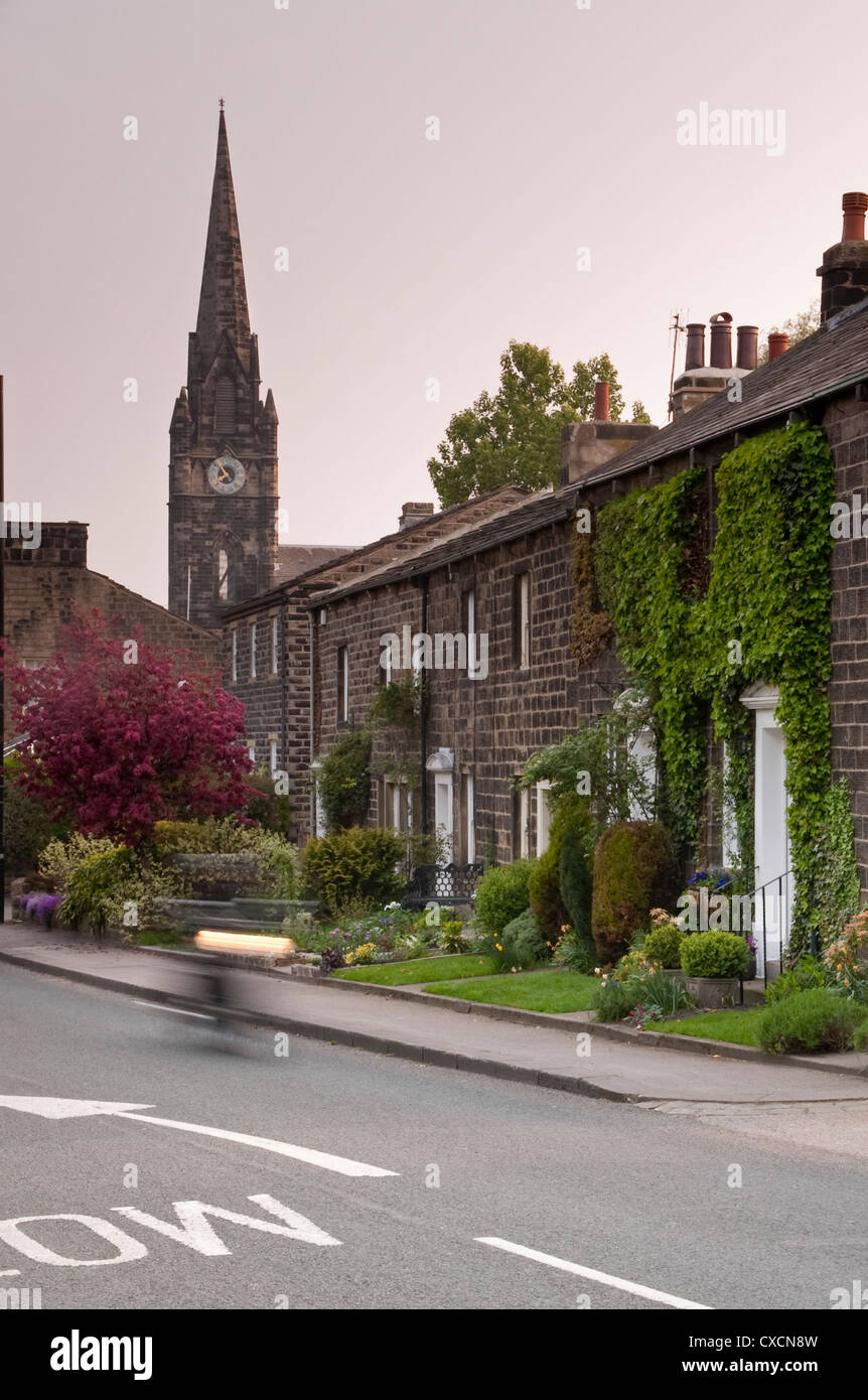 Terrasse Zeile aus Stein gebauten Cottages am Straßenrand mit hoch aufragenden Turm & Uhr der St. Mary's Kirche jenseits - Burley-in-Wharfedale, Yorkshire, England, UK. Stockfoto