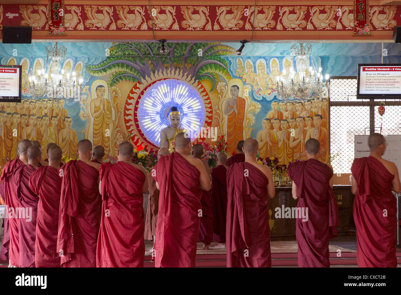 Buddhistische Mönche verehren Buddha im Tempel Altar mit Wandmalereien von Jüngern und Bodhisattvas Stockfoto