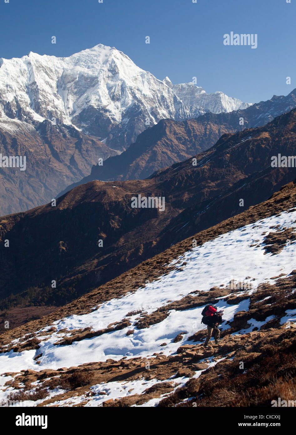 Nepalesische Porter eine Tragetasche und zu Fuß auf einem Hügel mit Schnee bedeckt, mit einem Hige schneebedeckten Berg in der Ferne, Nepal Stockfoto