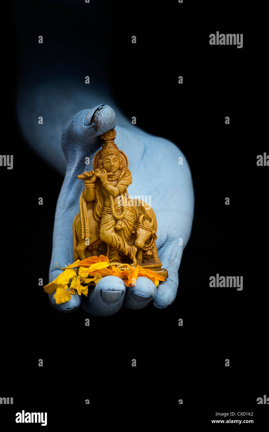 Blauen indischen mans Hand mit Lord Krishna Statue und Blume Blüten auf schwarzem Hintergrund Stockfoto