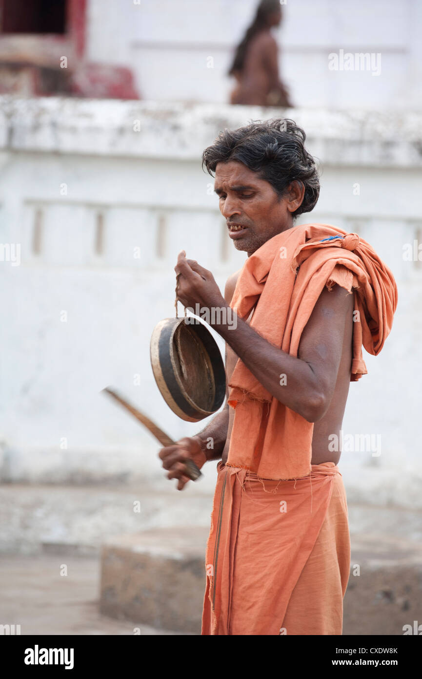 Joranda Mönch in der Abenddämmerung, tragen orange Tuch, ein Becken zu klingen, als Vorbereitung für rituelle Abendgebet, Joranda, Orissa, Indien Stockfoto