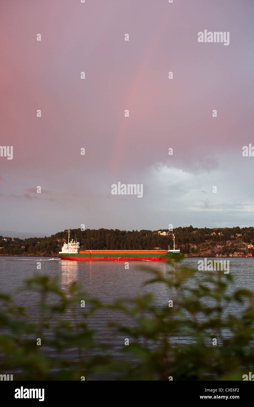 Ein Containerschiff unter einem Regenbogen Stockfoto