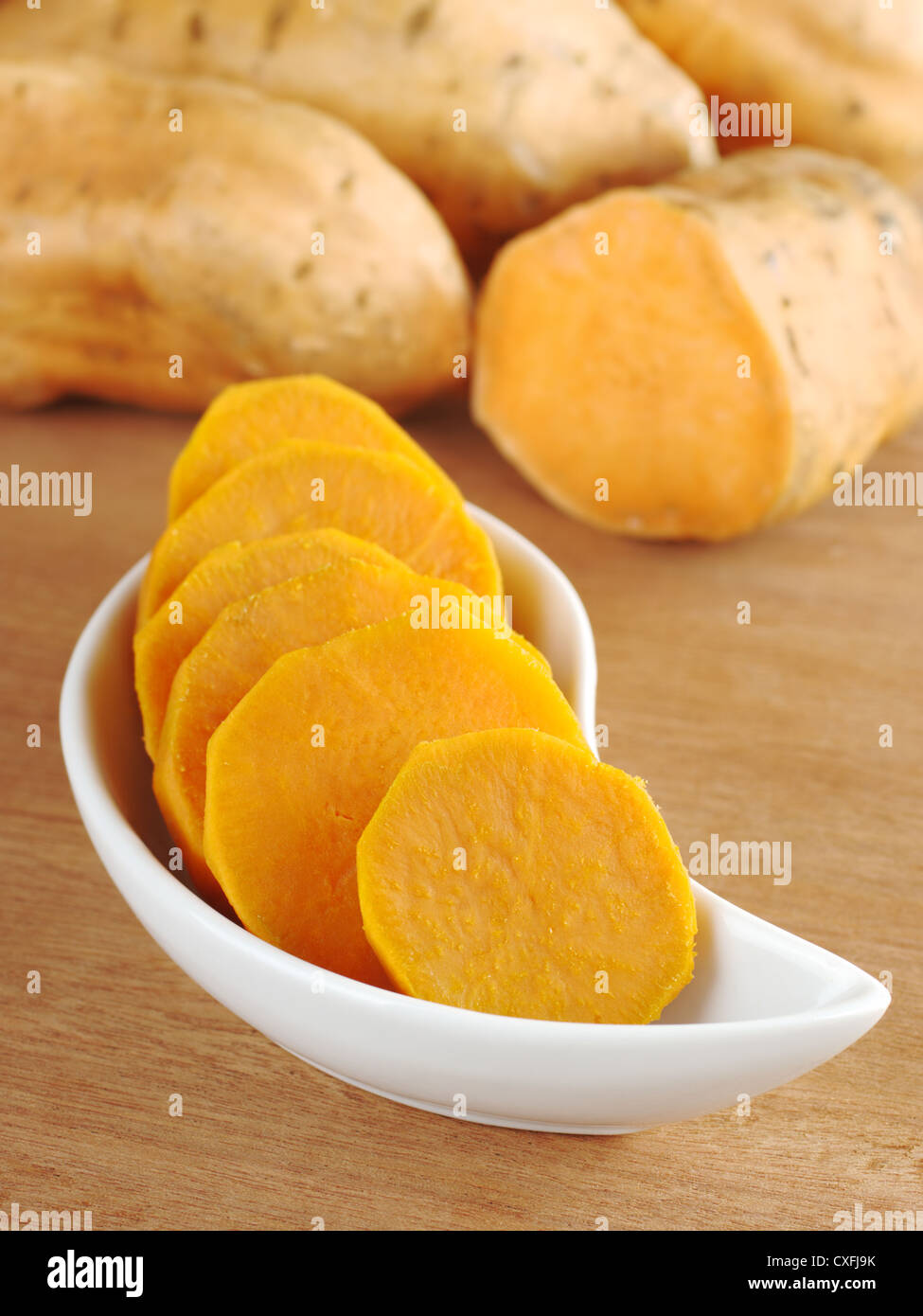Süßkartoffel (Ipomoea Batatas lat.) schneiden Sie in Scheiben in weiße Schüssel auf Holzoberfläche mit Süßkartoffeln im Hintergrund gekocht Stockfoto