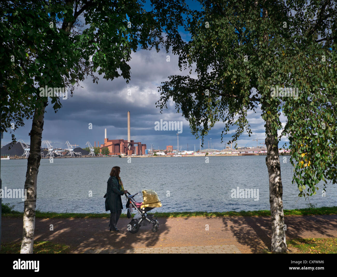 Kohlekraftwerk in fossilen Technologie von dramatischen Himmel mit Frau schieben Kinderwagen im Vordergrund Helsinki Finnland beleuchtet Stockfoto