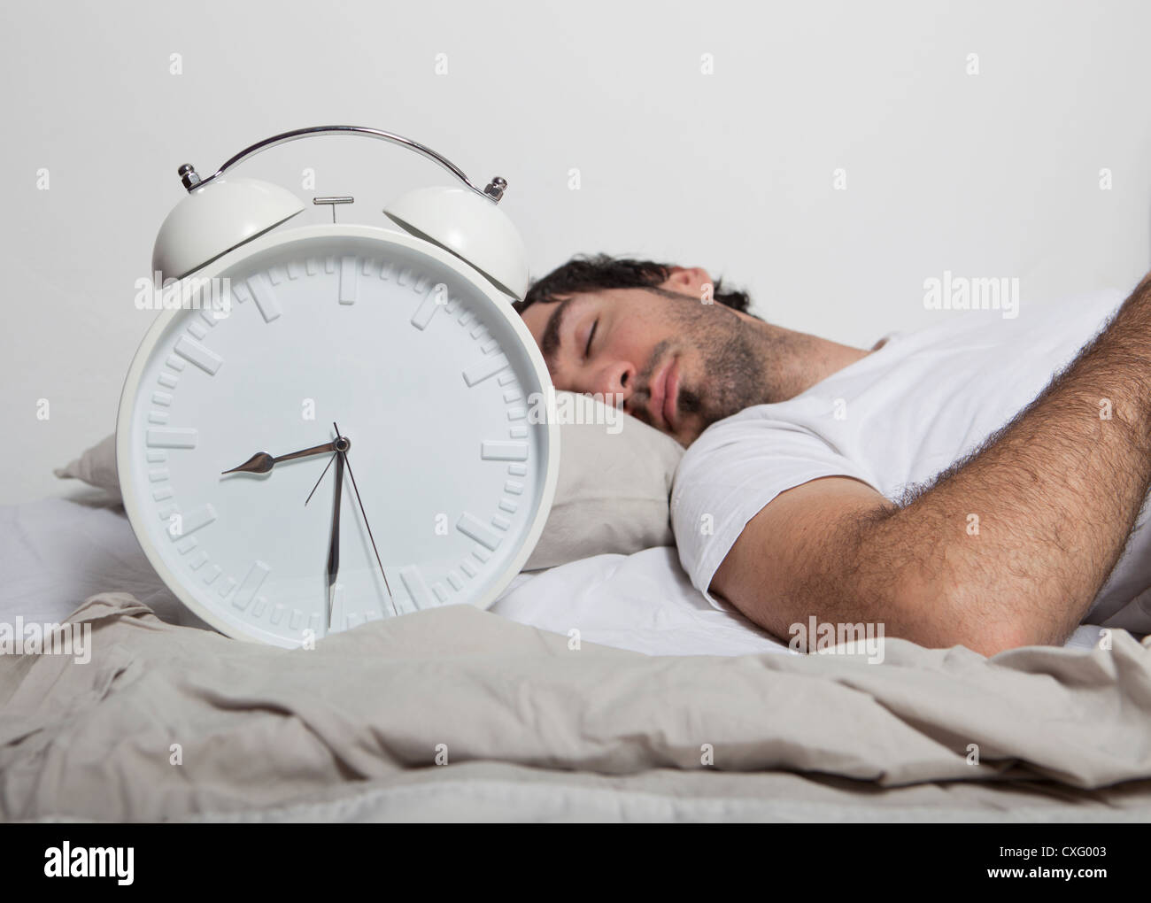 Ein Mann mit im Bett mit einem großen weißen Wecker. Stockfoto