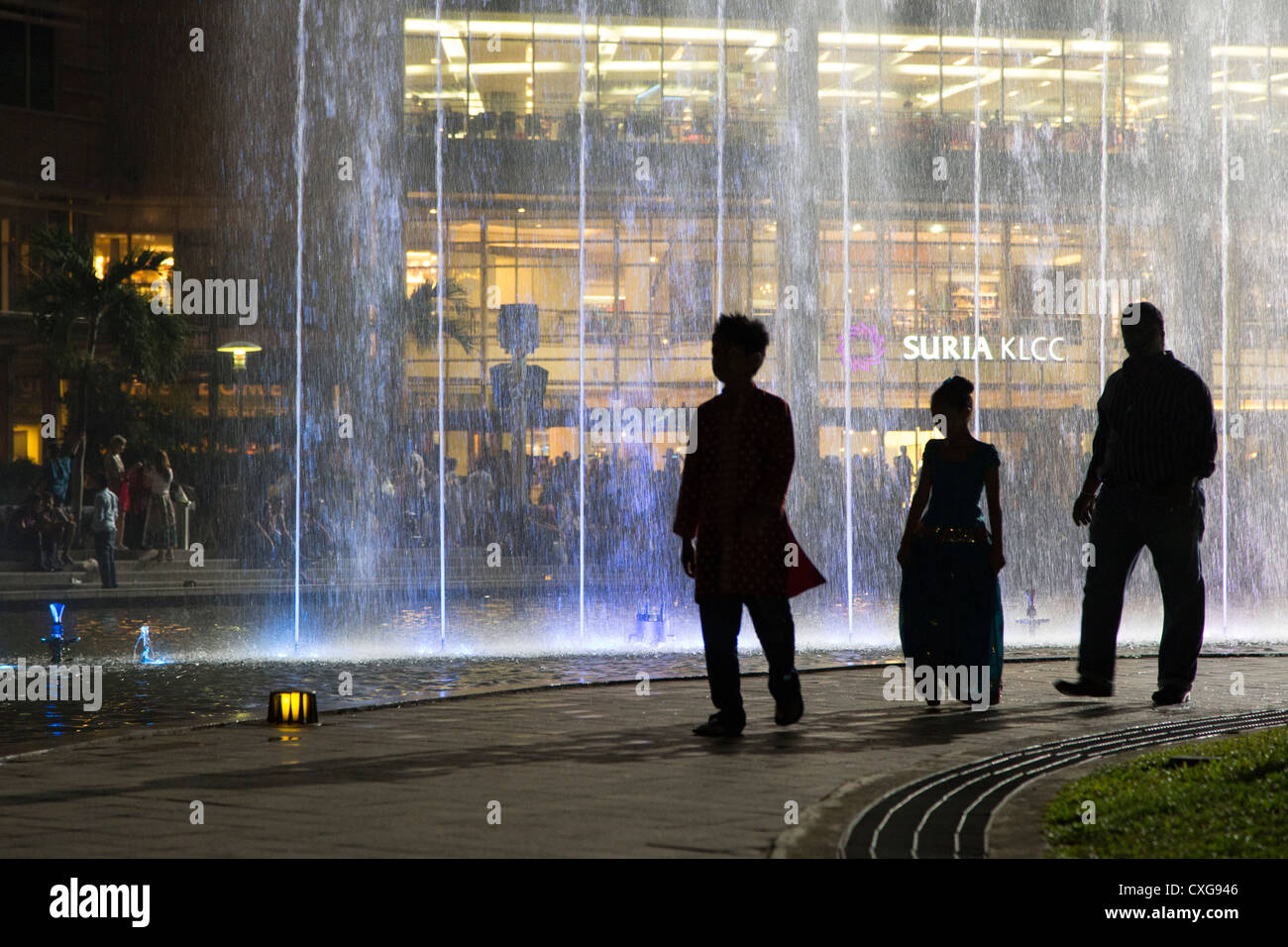 3 Personen (Silhouetten) zu Fuß vor einem modernen Brunnen in den Petronas Tower Park in Kuala Lumpur, Malaysia Stockfoto