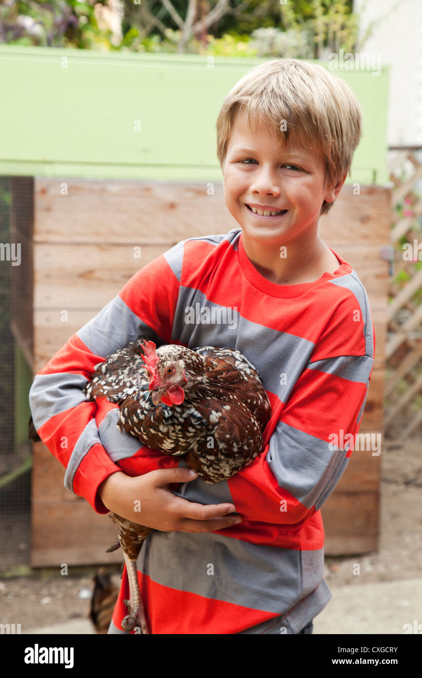 Ein Junge hält ein Huhn in seinem Hinterhof. Stockfoto