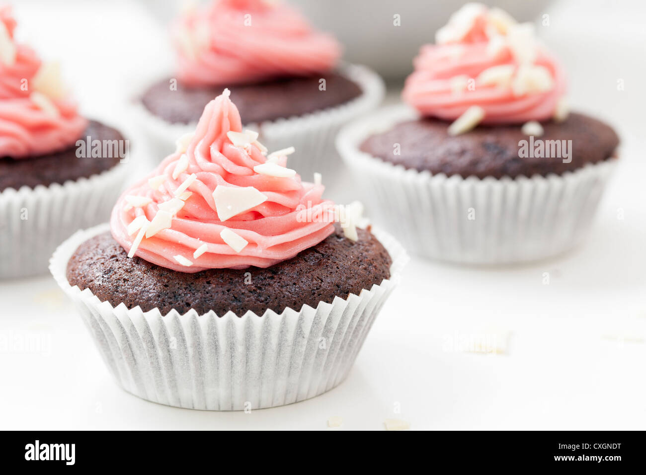 Schokolade Cupcake mit rosa Zuckerguss gekrönt und bestreut mit weißen Schokoladenflocken. Stockfoto