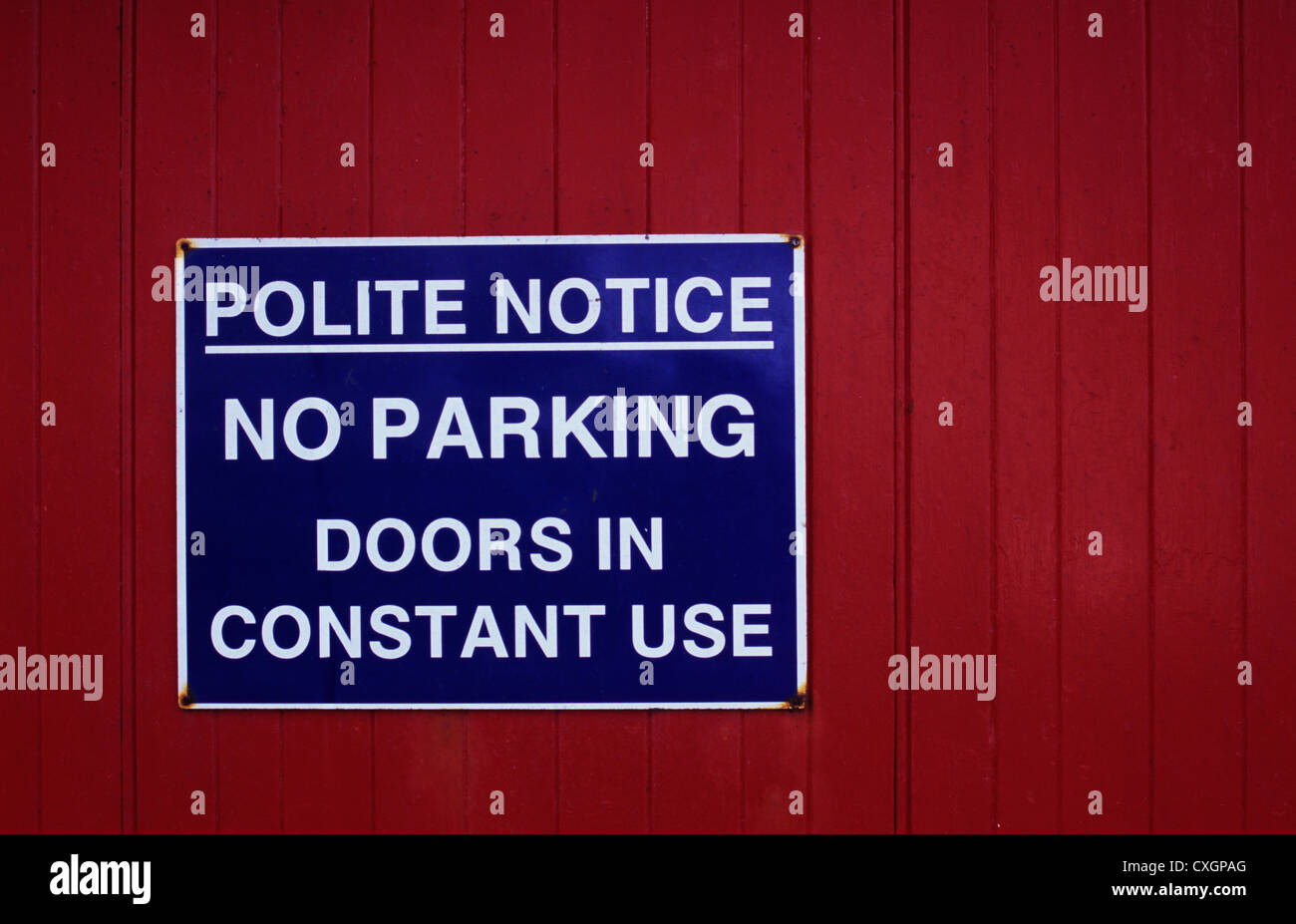 Blaue und weiße Bekanntmachung über rot bemalten Holztüren besagt höflichen Hinweis No Parking Türen im Dauereinsatz Stockfoto