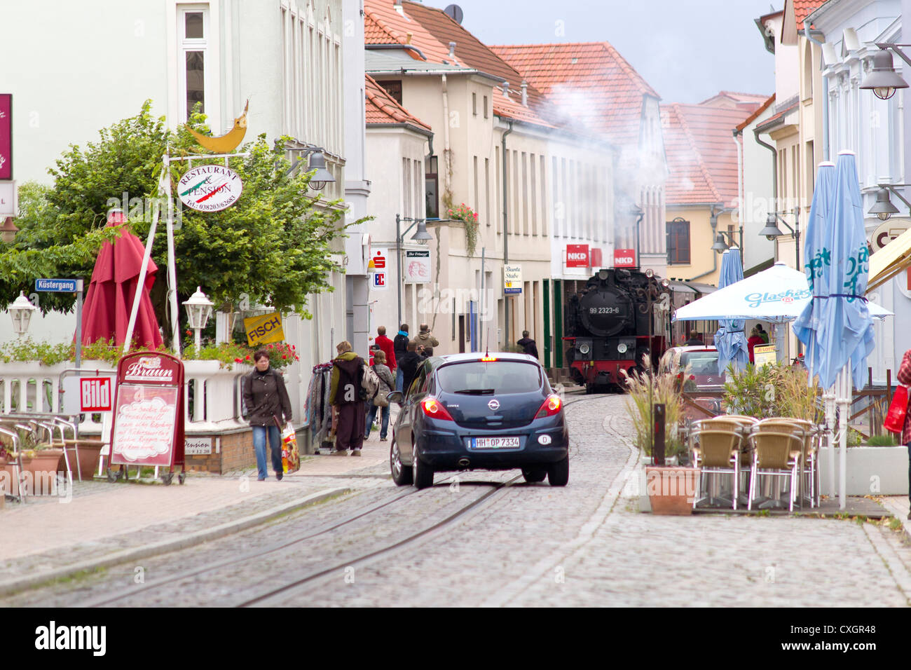 Dampflok zieht ein Passagier Zug und einem Auto auf der Straße. Der Molli-Bahn in Bad Doberan - Deutschland Stockfoto