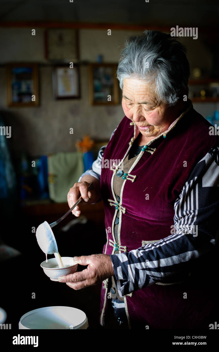 Mongolische Seniorin gießt hausgemachtes traditionellen Joghurt in Schüssel in ihrem ländlichen Zuhause Stockfoto