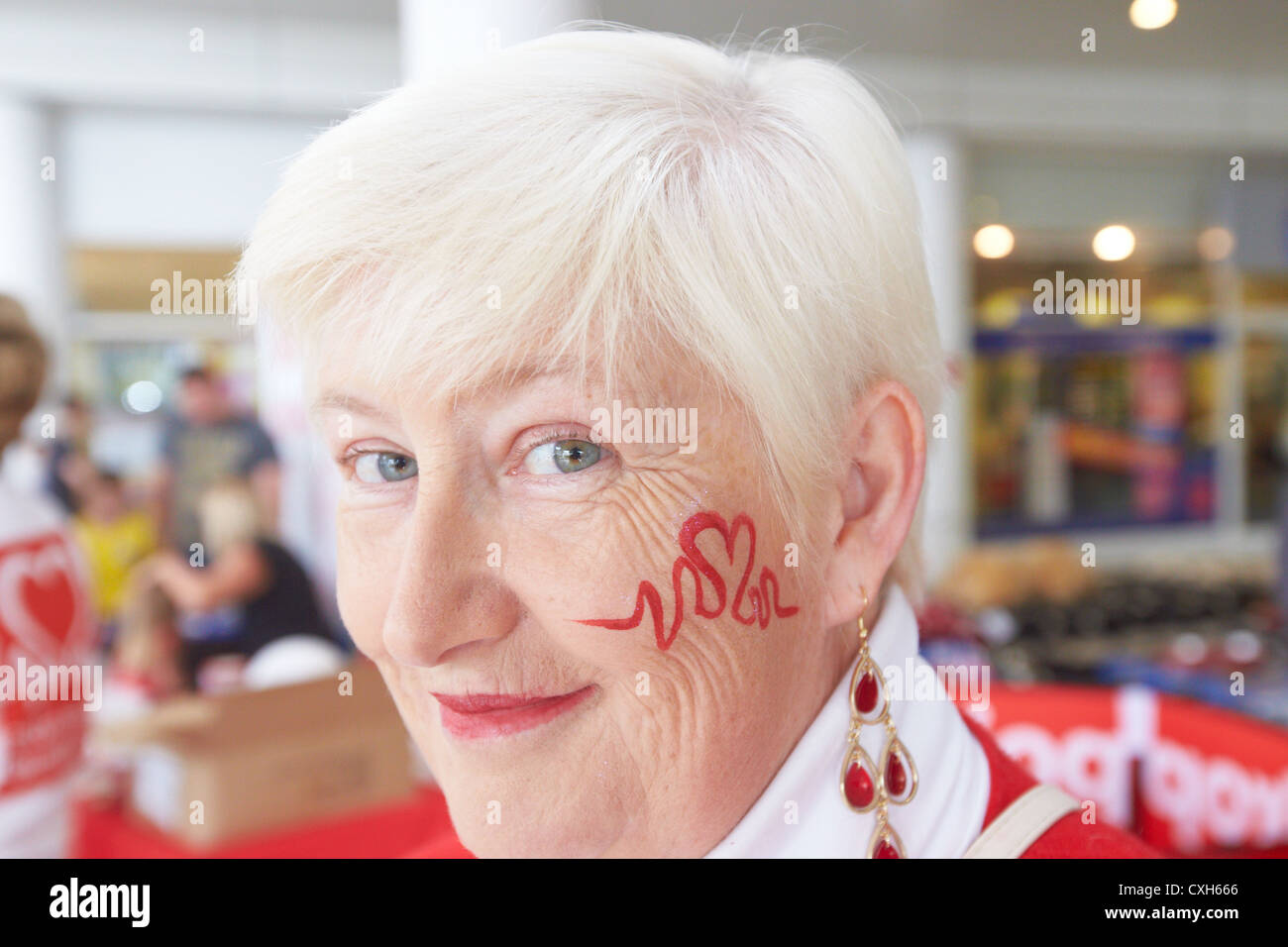 Mary Clifford, Freiwilliger für die British Heart Foundation, mit der Charity Logo auf ihrem Gesicht. Stockfoto