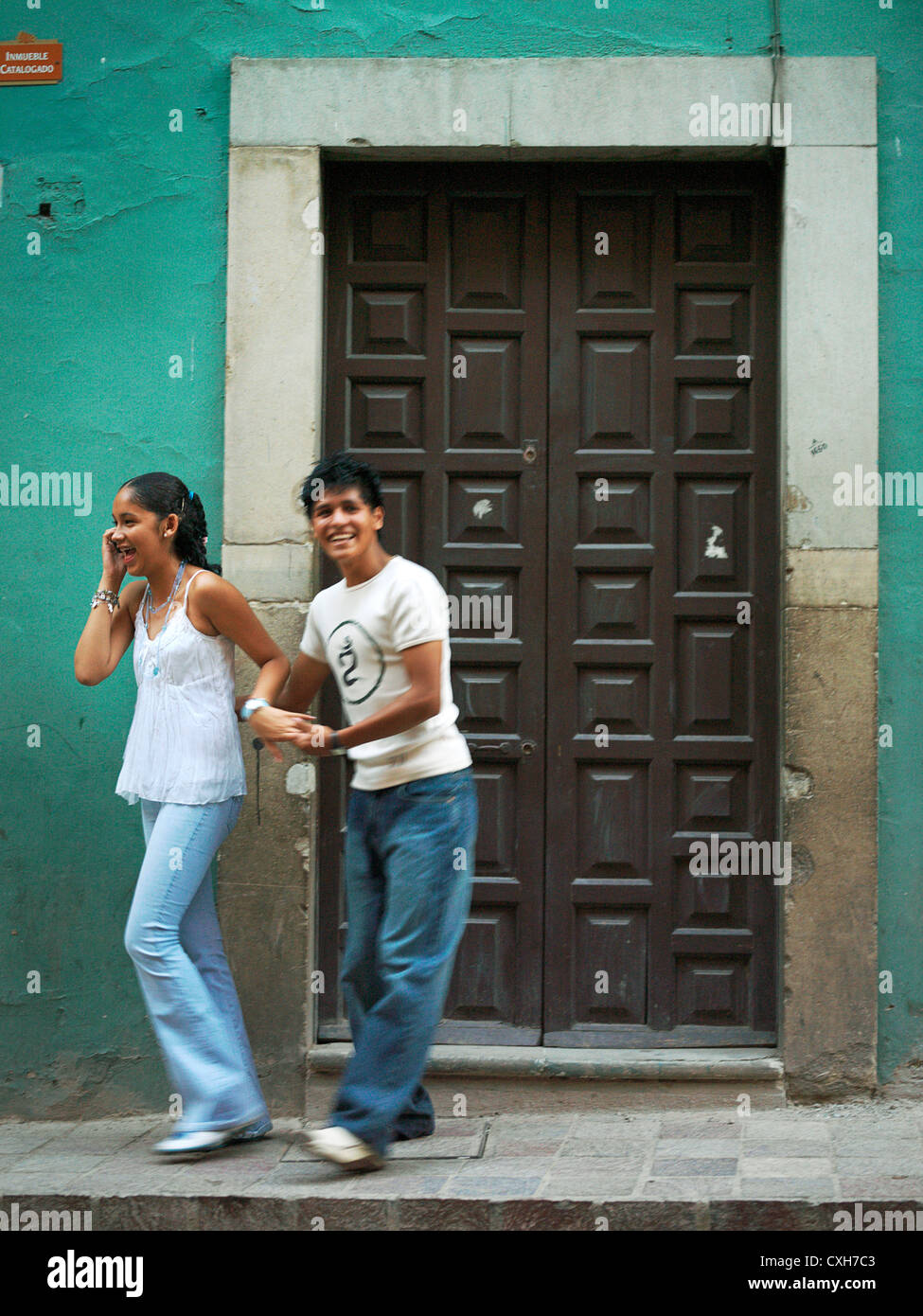 Edgar Israel und Ixbel Ixta, ein junger, lächelnd, späten Teenager Paar, in einer Straße. Ixbel ist auf ihrem Handy chatten. Modell rele Stockfoto