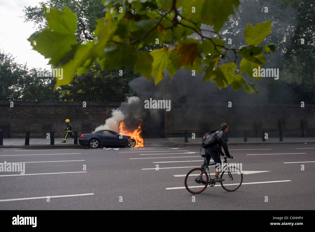 Ein Radfahrer Pedale Vergangenheit ein Mercedes wie es brennt an der Seite der Straße am Hyde Park Corner im Zentrum von London. Stockfoto