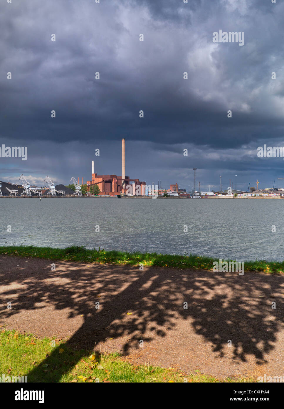 GREEN FUTURE CONCEPT Kohlekraftwerk fossile Brennstoffe alte Technologie unter dramatisch grübelnden Himmel mit Baum und Blättern im Vordergrund Stockfoto