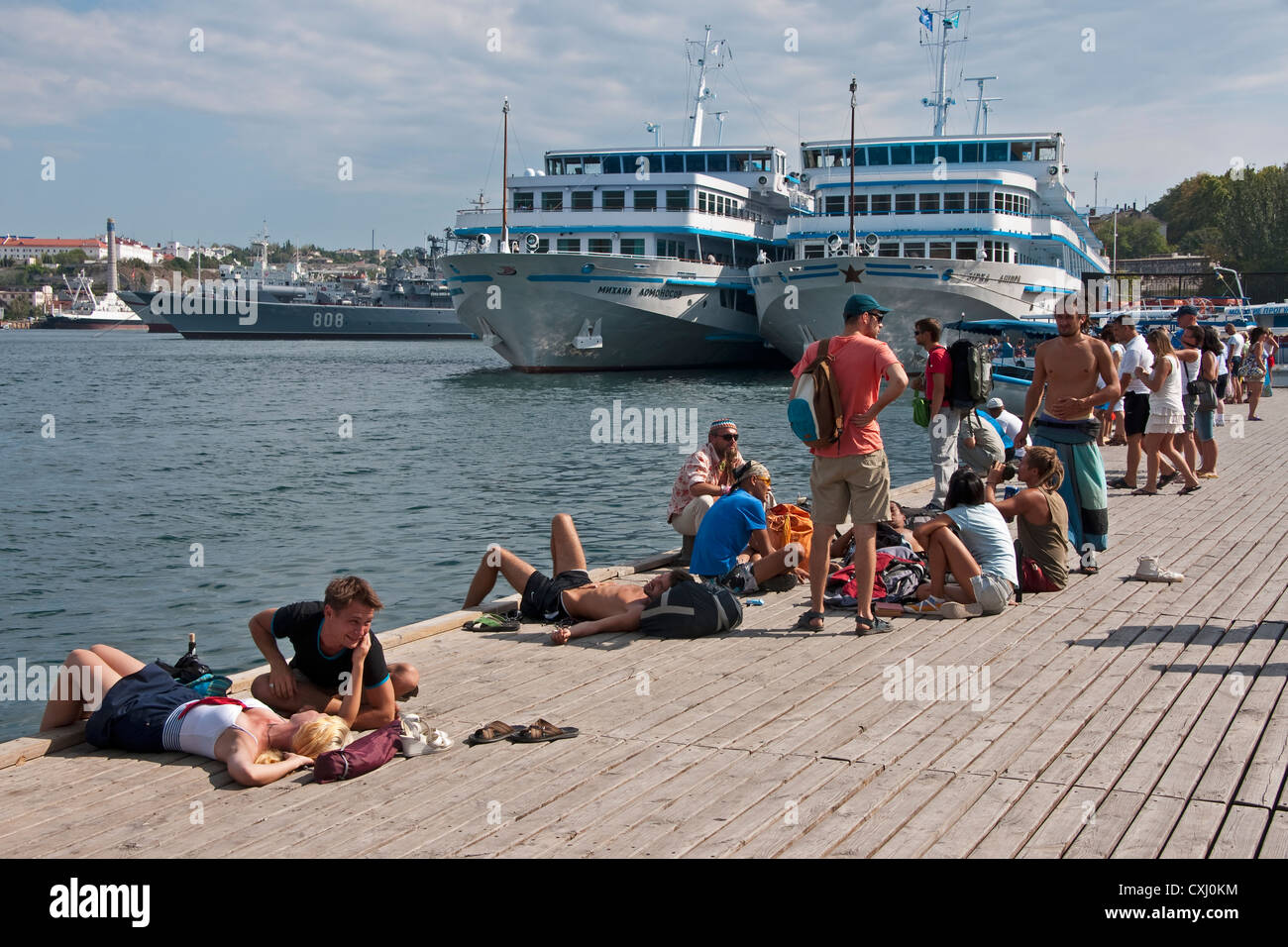 Junge Rucksacktouristen auf Grafs Kai im Hafen von Sewastopol mit Marine und Kreuzfahrtschiffe im Hintergrund. Stockfoto